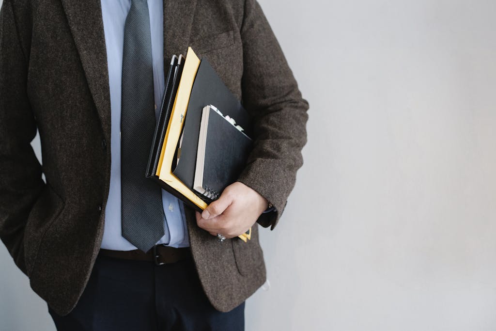 Business professional in a suit holding various folders and notebooks indoors.