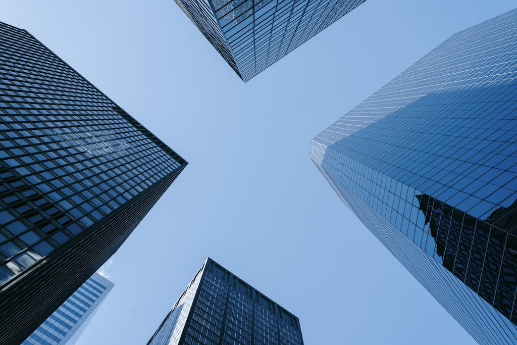 Low angle of high business towers with glass mirrored windows located in megalopolis downtown against blue sky