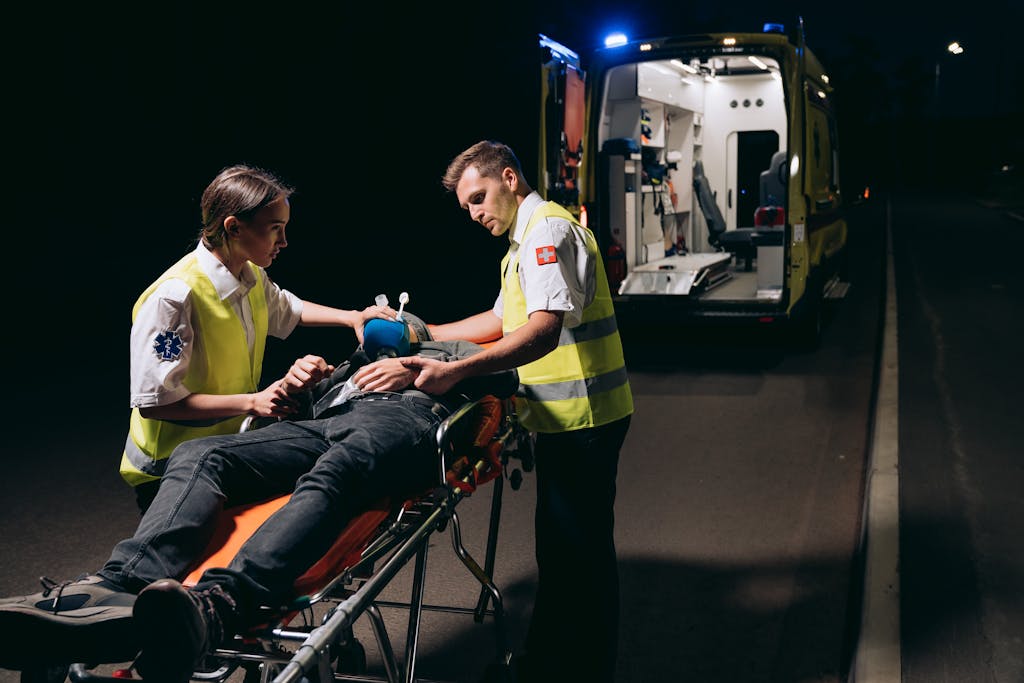 Paramedics attending to a patient on a stretcher with an ambulance nearby at night.
